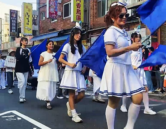 耶穌基督後期聖徒教會傳教士穿著白色水手服參與2025淡水藝術嘉年華踩街遊行，與「錫安號」花車合影，沿街與民眾互動合影，場面熱烈